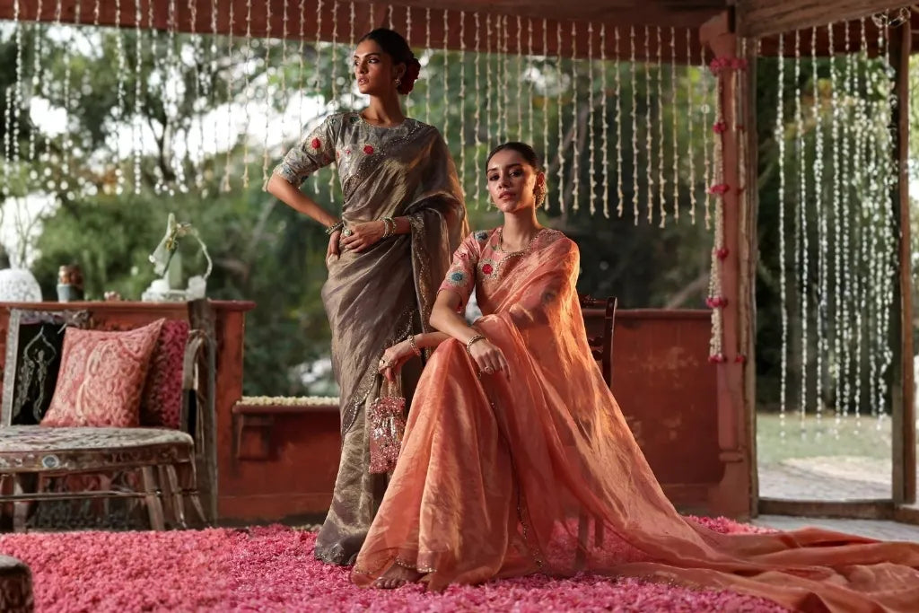 Two women wearing elegant grey and peach embroidered sarees with traditional styling for festive occasions and celebrations.