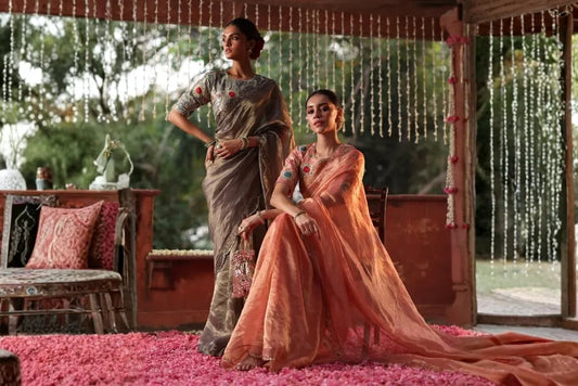 Two women wearing elegant grey and peach embroidered sarees with traditional styling for festive occasions and celebrations.